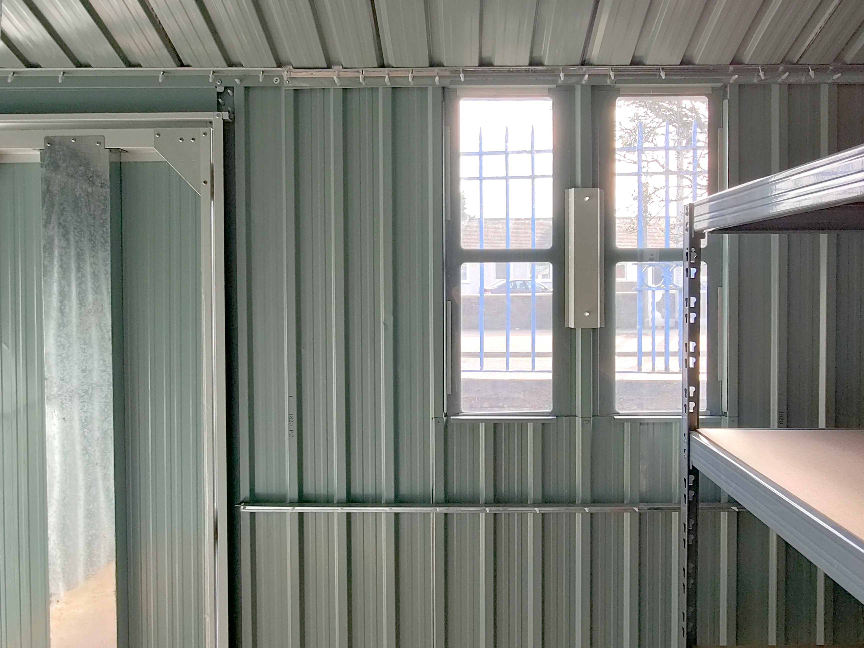 a view of the window on the cottage shed as seen from inside the shed. The white-grey brace bar which holds it against the shed wall is visible.