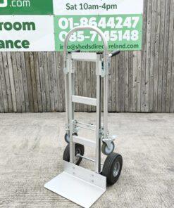 The 2 in 1 hand truck in the upright hand truck position against a wooden wall
