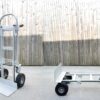 The 2 in 1 trolley seen in both it's positions. On the left it stands as a hand trolley on the right it sits as a flatbed trolley. It's silver and slightly matted with black wheels and handles.