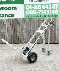 the three in one hand truck in the horizontal position. The extendable arm is also fully extended. The unit is a shiny grey metal and it stands against a wooden wall