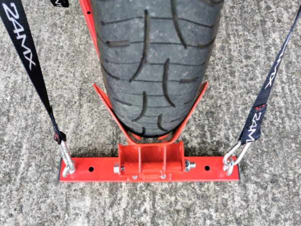 A top down view of the stand, showing the wheel in the back port. There are black and red cable straps holding the wheel securely in position. There are deep traction grooves on the wheel.