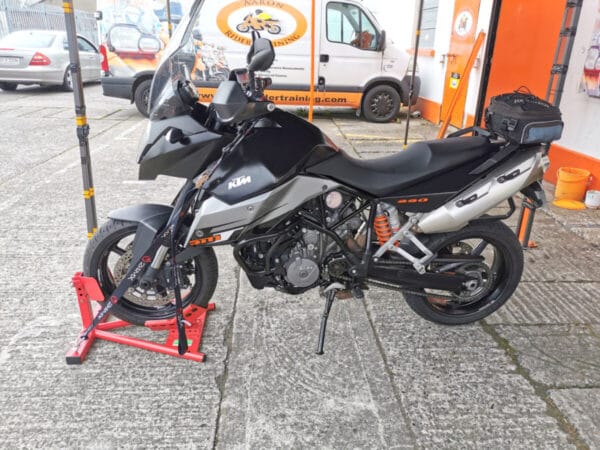 A side view of the motorbike on the stand. There are straps holding the bike in place and the bike stand is suspender, i.e. it is not touching the ground