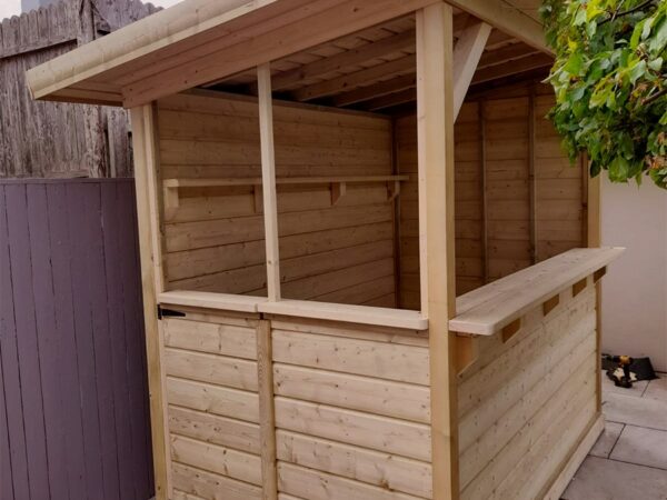 The side aspect of the wooden garden bar where the door is. The roof is clearly sloping from front to back