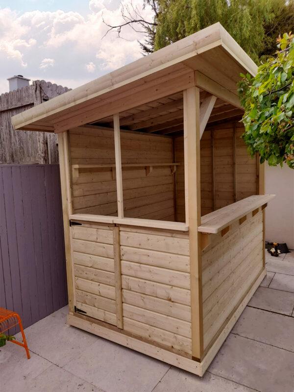 The side aspect of the wooden garden bar where the door is. The roof is clearly sloping from front to back