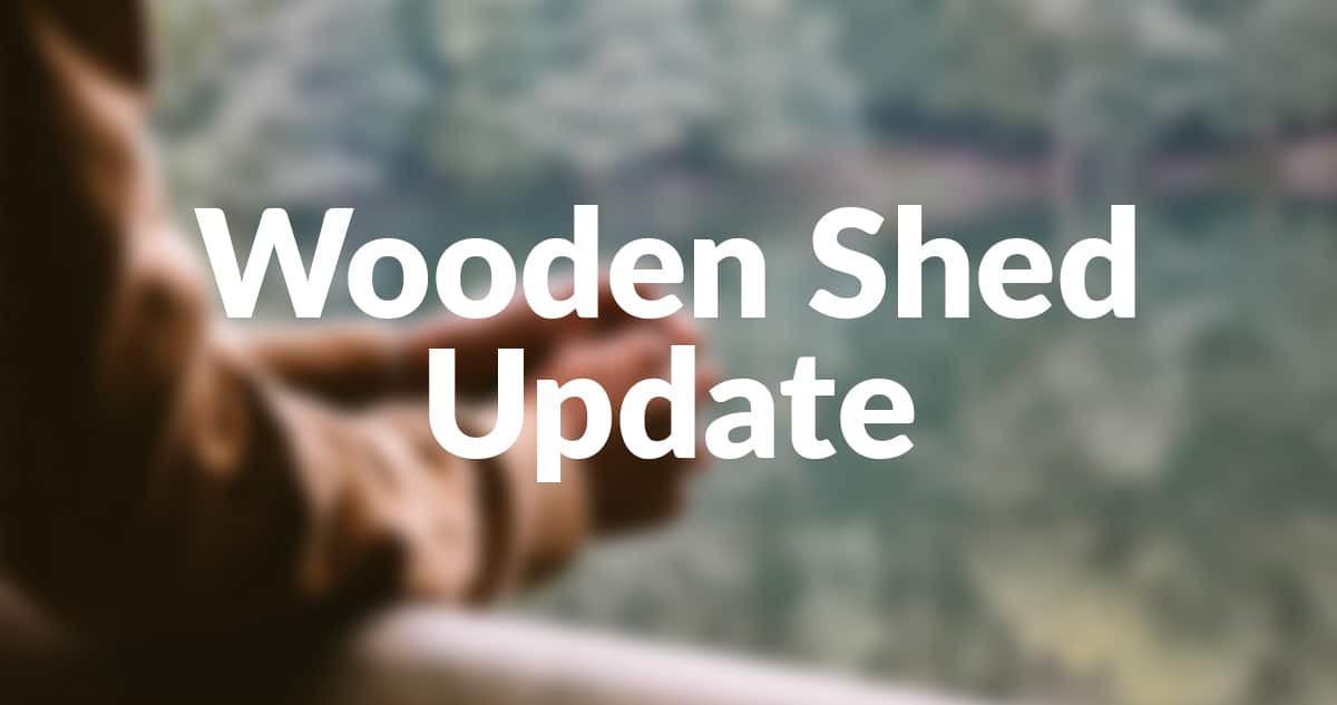 A picture of a pair of hands clasped together on the veranda of a wooden shed. The image is blurred and sharp letters sit on top that read 'Wooden Shed Update'