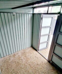Inside the Premium Pitched Steel Garden Shed. It has no floor and the pebblestones are visible as the base. The door is open and light pours in through it and also from the large window above the door