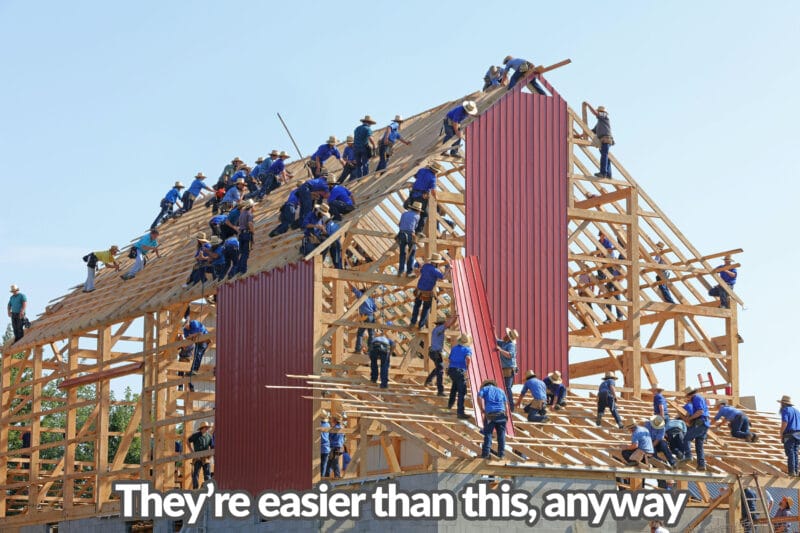 At least 40 Amish men in light blue shirts and dark blue pants are standing on an enormous shed structure, piecing it together. Some are holding wooden panels, others are holding pieces of paper and some and are hammering nails. It reads 'well, it's easier than this anyway'