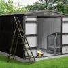 The Premium Apex 8ft x 10ft steel premium garden shed in a garden. The doors are both open and inside there is a workbench and a yellow lawnmower. Outside a large, black ladder is open to the left hand side of the image and there are small tools in the built in tool hooks on the doors