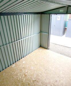 Inside the 8ft x 10ft steel premium garden shed. The view is from high in the top corner looking outwards to the door, which is on the right side of the frame. The walls are a light grey and they have a brace bar running along the centre
