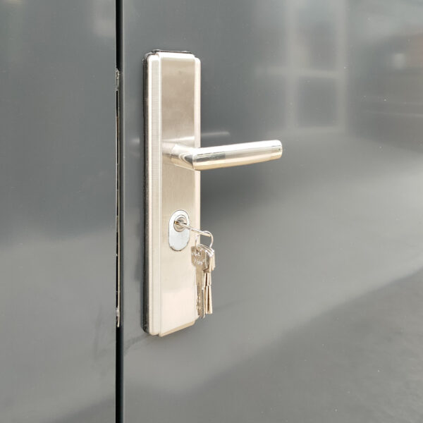 The built in handle lock of the premium shed. It is a pale silver with a long, protruding handle above the keyhole. The walls of the shed are an anthracite grey colour