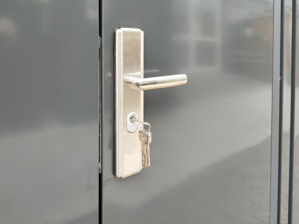 The built in handle lock of the premium shed. It is a pale silver with a long, protruding handle above the keyhole. The walls of the shed are an anthracite grey colour