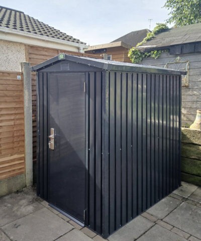The shed is at an angle in the garden, the door and side panels are visible. There is a concrete base beneath it.