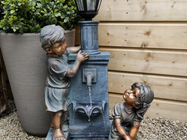 The Grandchildren Water Feature against a white background and with a green plant pot beside it