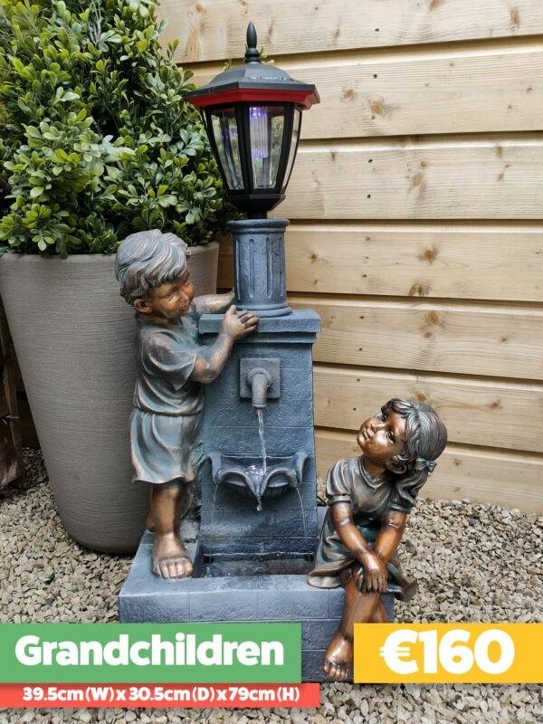 The Grandchildren Water Feature against a white background and with a green plant pot beside it