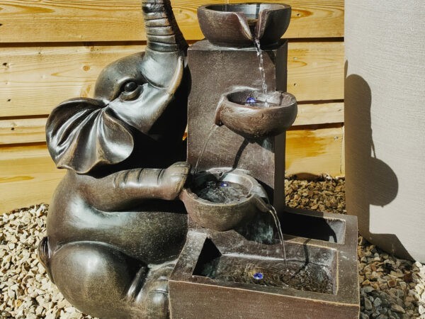 The Jumbo water feature. It is a bronze elephant up against a wooden shed with a plant behind it. The water pours out of the elephants trunk.