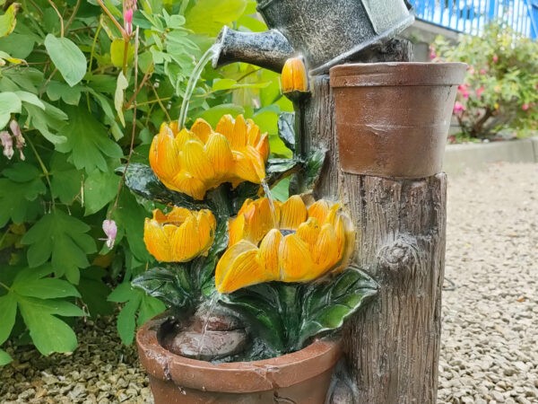The sunflowers water feature. It shows a silver watering can on top of a faux wooden plinth. The can is pouring water into one sunflower and the water is running down, through two of the petals into another smaller one, which does the same, except that it pours into the base. The base is a terracotta style plant pot