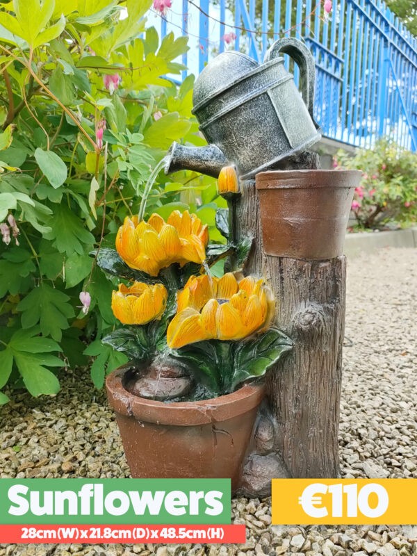 The sunflowers water feature. It shows a silver watering can on top of a faux wooden plinth. The can is pouring water into one sunflower and the water is running down, through two of the petals into another smaller one, which does the same, except that it pours into the base. The base is a terracotta style plant pot