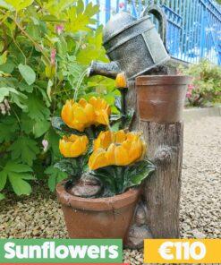 The sunflowers water feature. It shows a silver watering can on top of a faux wooden plinth. The can is pouring water into one sunflower and the water is running down, through two of the petals into another smaller one, which does the same, except that it pours into the base. The base is a terracotta style plant pot