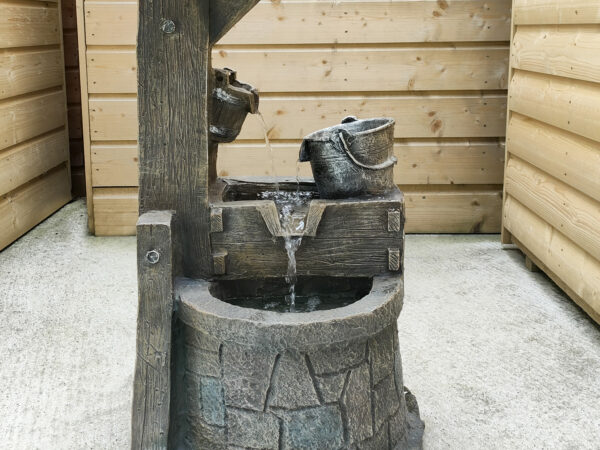 The Wishing Well water feature on the balcony of a wooden chalet shed. The wishing well has an awning above it and a bucket on a rope to the side