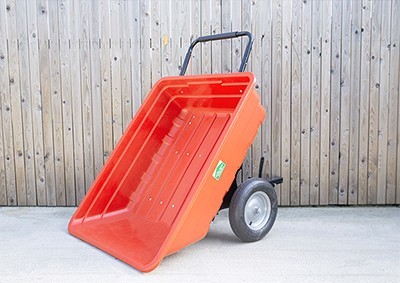 A large, red garden cart tipped down against a wooden wall