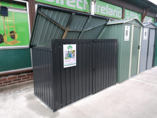 The bin store as seen from a 45 degree angle. The lid is open showing the paler grey colour that is on the inside. The unit itself is a dark grey and there is a white rectangular piece of paper on the front of it while denote the details of the shed to customers