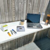 The Balcony Table filled with items including a laptop, a large book, a box of crisps, pens, a stationary holder, a coffee cup and pens.