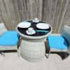 An aerial view of the fold in table and chairs set. There are bright blue cushions on the chairs, two large white plates and white cups and saucers on the table