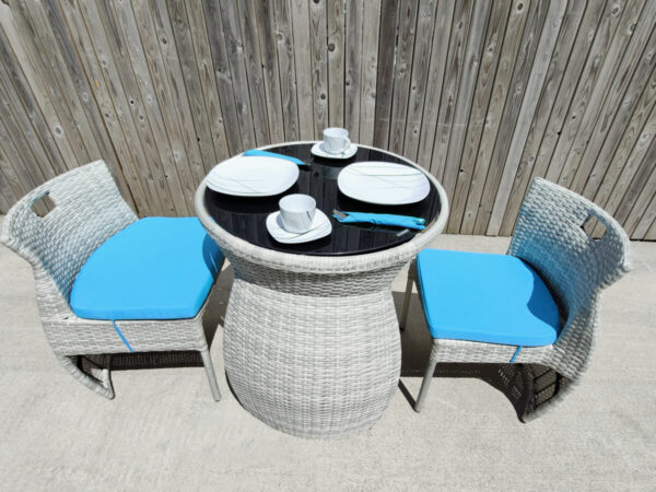 An aerial view of the fold in table and chairs set. There are bright blue cushions on the chairs, two large white plates and white cups and saucers on the table