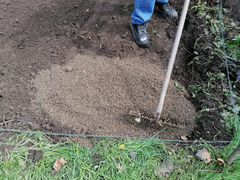 Laying a base for a steel shed: the gravel has been poured into the pit and it is being flattened by a rake