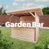 A wooden Garden Bar with a back wall, a side wall and a low bar front and no wall to the fourth side. It is a pale, golden brown and the sun is setting behind it. In the foreground, there is the leaves of a large, green tree