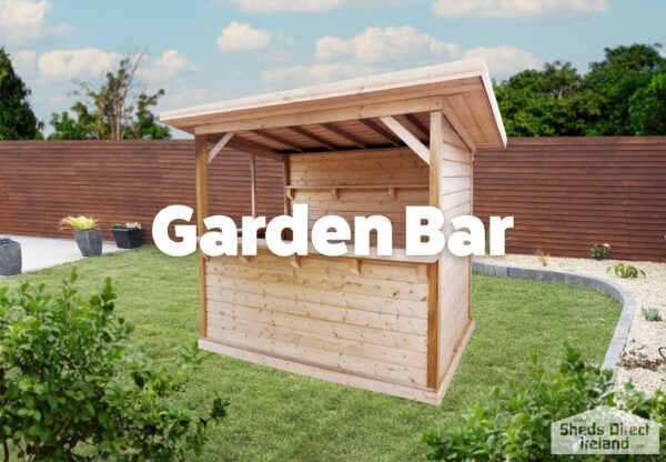 A wooden Garden Bar with a back wall, a side wall and a low bar front and no wall to the fourth side. It is a pale, golden brown and the sun is setting behind it. In the foreground, there is the leaves of a large, green tree