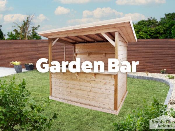 A wooden Garden Bar with a back wall, a side wall and a low bar front and no wall to the fourth side. It is a pale, golden brown and the sun is setting behind it. In the foreground, there is the leaves of a large, green tree