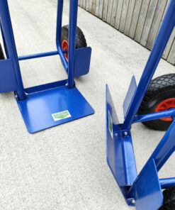 The folding footplate on the blue hand truck. Two trollies are side by side, one has the footplate down, the other has it up
