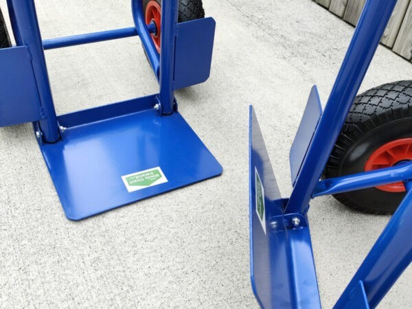 The folding footplate on the blue hand truck. Two trollies are side by side, one has the footplate down, the other has it up
