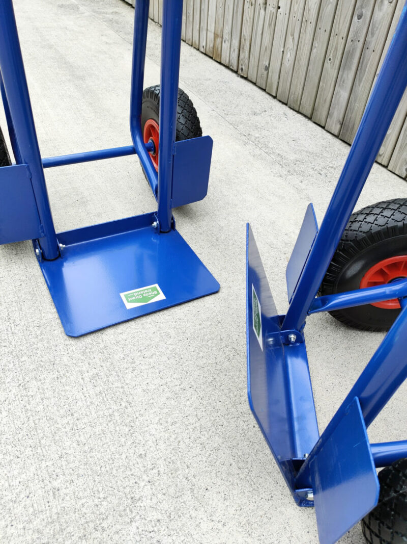 The folding footplate on the blue hand truck. Two trollies are side by side, one has the footplate down, the other has it up