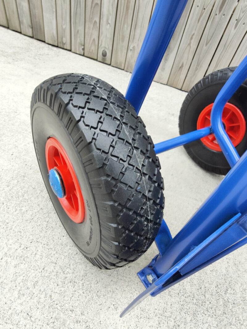 A close up view of the hard tyres on the blue hand truck. The tyres are a hard plastic and they have an internal red metal rim with a bright blue protective cap covering the centre