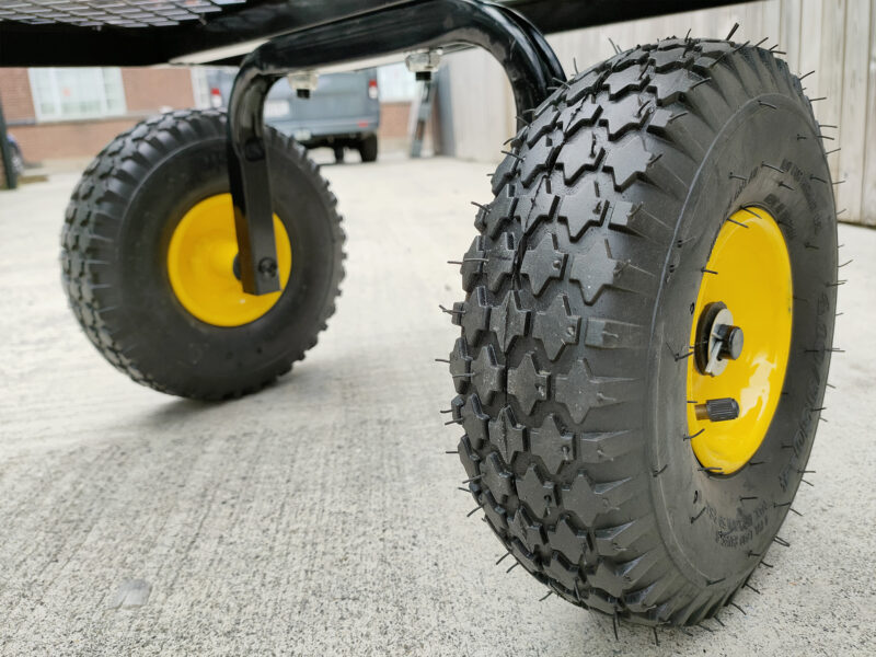A close up view of the thick tyres on the mesh cart. They are black rubber with an internal, bright yellow rim. They have thick grooves and they are 25cm in diamter and they are 8cm thick.