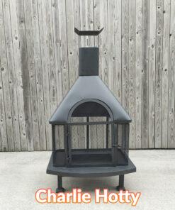 The Charlie Hotty Fire pit as seen face on from a relatively low height. It is a squat, square base fire-pit supported by 4 legs and it has a chimney above the fire pit.