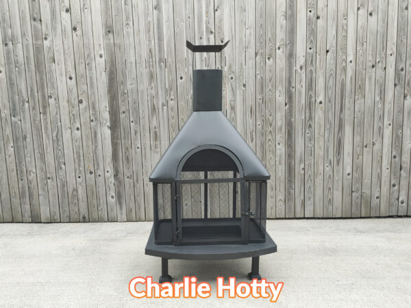 The Charlie Hotty Fire pit as seen face on from a relatively low height. It is a squat, square base fire-pit supported by 4 legs and it has a chimney above the fire pit.