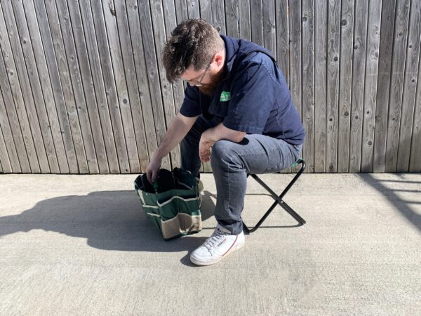 Sean from Sheds Direct Ireland sitting on the chair from the garden tool bag with chair set, reaching into the bag pulling out a trowel