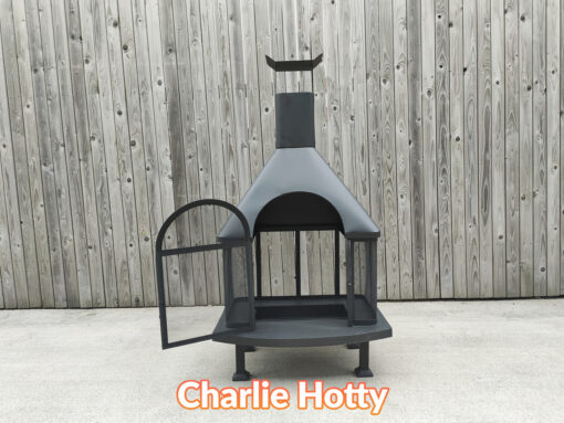 The charlie hotty fire pit asseen with the grate door open. It is a large, squat, black firepit against a wooden wall