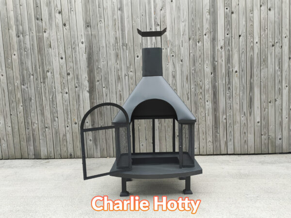 The charlie hotty fire pit asseen with the grate door open. It is a large, squat, black firepit against a wooden wall