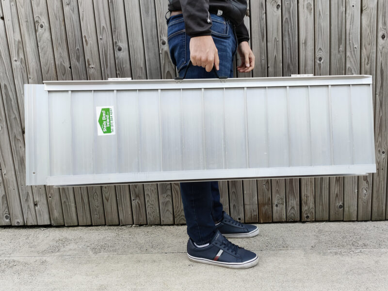 The Medium Wheelchair Ramp being held by a man in a navy shirt, dark jeans and navy shoes. He is holding the ramp in one hand. It looks heavier in his arms than the small, but he still seems relatively unphased.