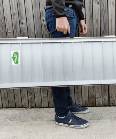 The Medium Wheelchair Ramp being held by a man in a navy shirt, dark jeans and navy shoes. He is holding the ramp in one hand. It looks heavier in his arms than the small, but he still seems relatively unphased.