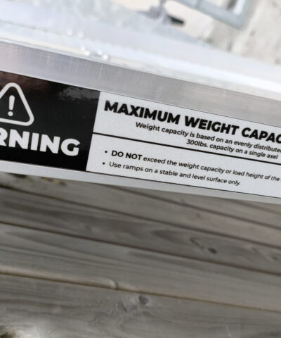 The warning sticker on the side of the ramp. It reads: MAXIMUM WEIGHT CAPACITY 600LBS. Weight capacity is based on an evenly distributed load on 2 axles. 300lbs capacity on a single axel. Do not exceed the weight capacity or load height of the ramp. Use ramps on a stable and level surface only'