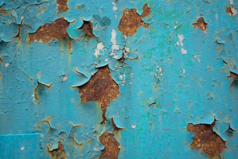 a close up of a piece of metal which was painted a teal-blue colour, but which now has large pockets of brown rust cutting through the paint