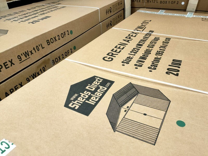 A pile of pale brown flat-packed boxes with 'GREEN APEX 9 FOOT X 10FT' written in black text on the top