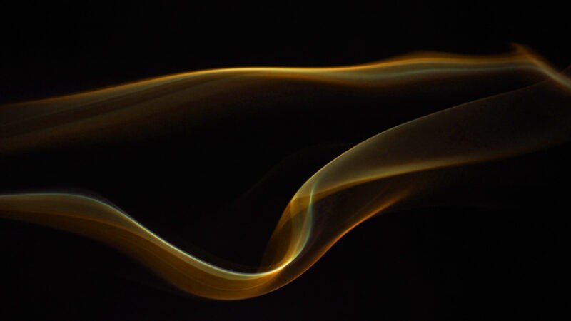 Smoke fumes moving in a horizontal line. They are lit by an orange light against a black backdrop