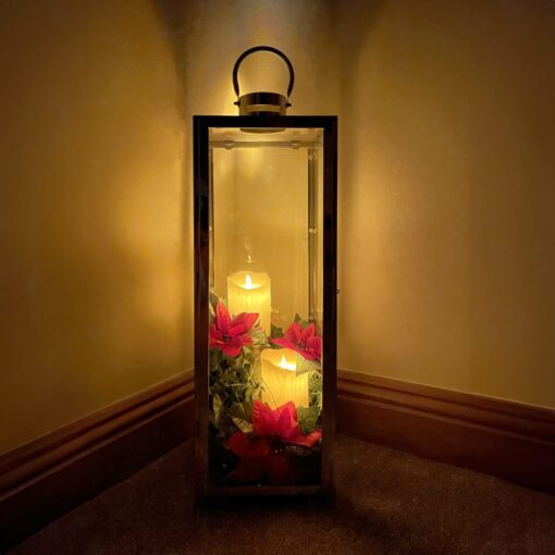 A lantern candle holder with two candles inside against a yellow wall