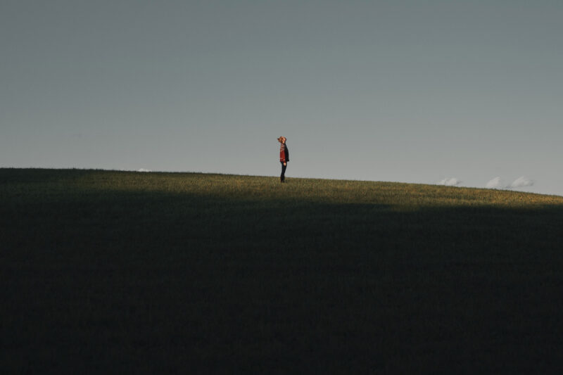 A full-length photo of a lone man on a hill in a red jumper with his head tilted back taking a big deep breath